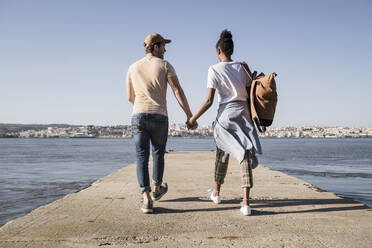 Junges Paar, das auf dem Pier am Wasser spazieren geht, Lissabon, Portugal - UUF19082