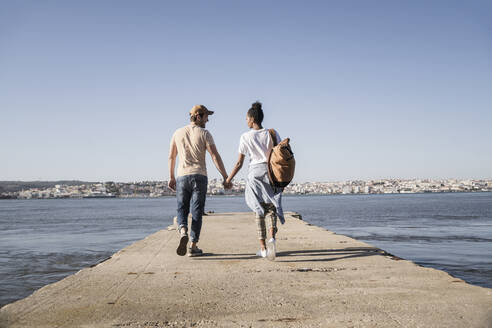 Young couple walking on pier at the waterfront, Lisbon, Portugal - UUF19083