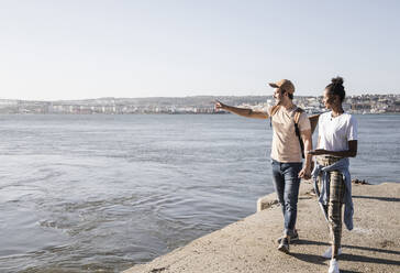 Young couple walking on pier at the waterfront, Lisbon, Portugal - UUF19098