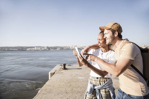 Junges Paar telefoniert am Pier am Wasser, Lissabon, Portugal, lizenzfreies Stockfoto
