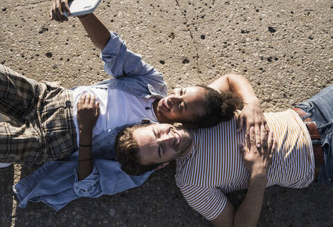 Glückliches junges Paar liegt auf Betonboden und macht ein Selfie - UUF19111