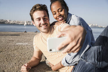 Glückliches junges Paar macht ein Selfie auf dem Pier am Wasser, Lissabon, Portugal - UUF19117