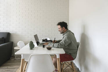 Man sitting at table working on graphics tablet and laptop - AHSF01031