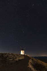 Spanien, Provinz Toledo, Consuegra, Sternenhimmel über einer alten Windmühle auf einem Hügel bei Nacht - WPEF02113