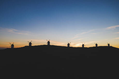 Spanien, Provinz Toledo, Consuegra, Silhouetten von Windmühlen, die in der Morgendämmerung auf einem Hügel stehen - WPEF02115