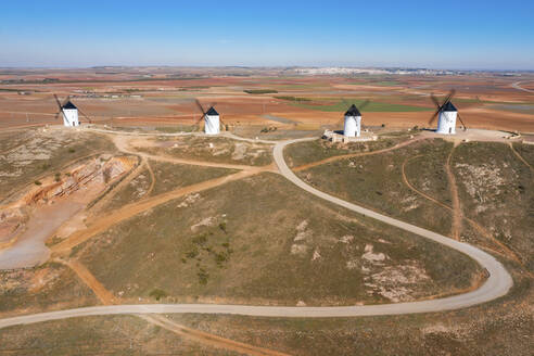 Spain, Province of Ciudad Real, Alcazar de San Juan, Winding road in front of old windmills standing on top of brown hill - WPEF02119