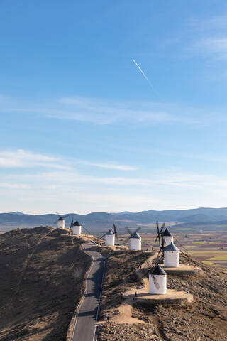 Spain, Province of Toledo, Consuegra, Country road along row of old windmills standing on top of hill stock photo