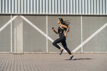 Young female jogger running in front of a wall - MTBF00035