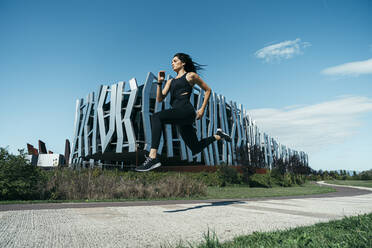 Junge Joggerin auf einem Weg vor einem modernen Gebäude - MTBF00044