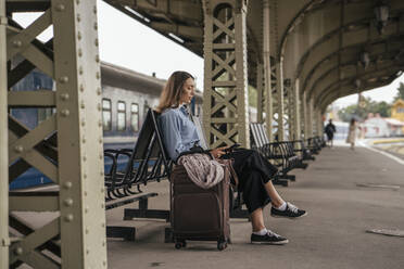 Junge weibliche Reisende, die auf dem Bahnhof wartet und ein E-Book benutzt - VPIF01730