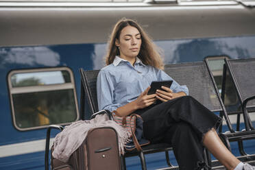 Young female traveller waiting on station, using e-book - VPIF01731