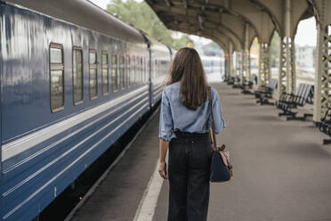 Rückansicht einer jungen weiblichen Reisenden auf dem Bahnsteig - VPIF01735