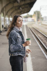Junge weibliche Reisende mit Kaffee zum Mitnehmen am Bahnhof - VPIF01739
