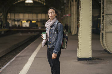 Junge weibliche Reisende mit Kaffee zum Mitnehmen auf dem Bahnsteig - VPIF01746