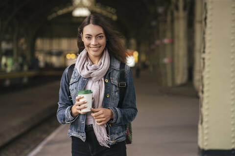 Junge weibliche Reisende mit Kaffee zum Mitnehmen auf dem Bahnhof, lizenzfreies Stockfoto