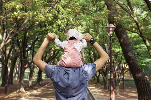 Vater, der mit einem kleinen Mädchen auf den Schultern in einem Park spazieren geht - GEMF03234