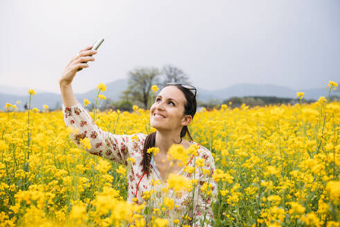 Porträt einer glücklichen Frau, die ein Selfie mit ihrem Smartphone in einem Rapsfeld macht, Gyeongju, Südkorea - GEMF03236