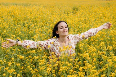 Portrait of happy woman with eyes closed and arms outstretched in a rape field - GEMF03237