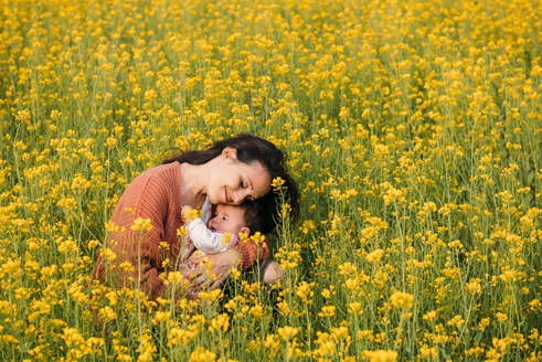 Glückliche Mutter, die mit ihrem kleinen Mädchen in einem Rapsfeld kuschelt - GEMF03240
