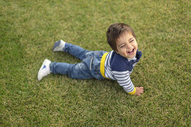 Porträt eines lachenden kleinen Jungen auf dem Rasen liegend - VGF00320