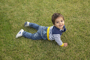 Portrait of smiling little boy lying on lawn - VGF00321