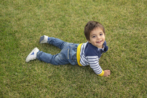 Porträt eines lächelnden kleinen Jungen auf dem Rasen liegend - VGF00321