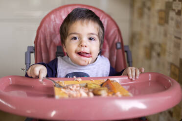 Portrait of little boy sitting on high chair eating vegetables - VGF00330