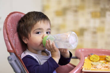 Porträt eines kleinen Jungen, der auf einem Hochstuhl sitzt und Wasser aus einem Flachmann trinkt - VGF00331