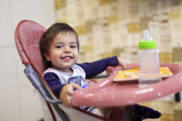 Porträt eines glücklichen kleinen Jungen, der auf einem Hochstuhl sitzt - VGF00333