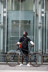 Stilvoller junger Mann mit Fahrrad und Umhängetasche in der Stadt - CJMF00151