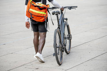 Junger Mann mit Umhängetasche, der ein Fahrrad schiebt - CJMF00162