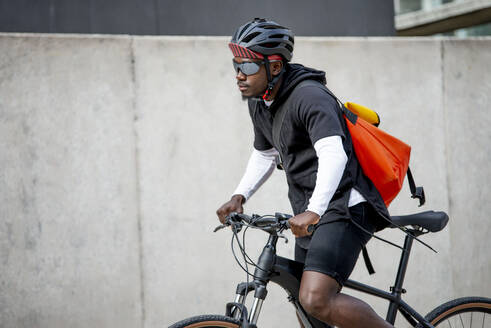 Stilvoller junger Mann mit Umhängetasche auf dem Fahrrad in der Stadt - CJMF00164