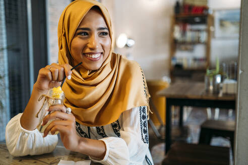 Junge muslimische Frau mit gelbem Hidschab in einem Cafe - MPPF00209