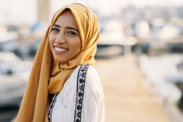 Junge muslimische Frau mit gelbem Hidschab beim Spaziergang am Hafen - MPPF00217