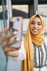 Young muslim woman wearing yellow hijab and using smartphone and taking a selfie - MPPF00239