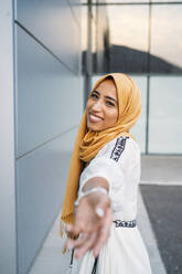 Junge muslimische Frau lächelt, trägt gelben Hijab und gibt ihre Hand - MPPF00240