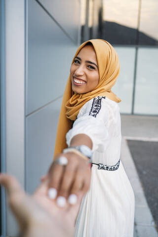 Young muslim woman smiling and taking hand of a man wearing hijab stock photo