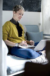 Portrait of woman sitting on couch using laptop - FLLF00328