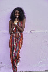 Portrait of young woman eating ice cream in front of purple wall - VEGF00782