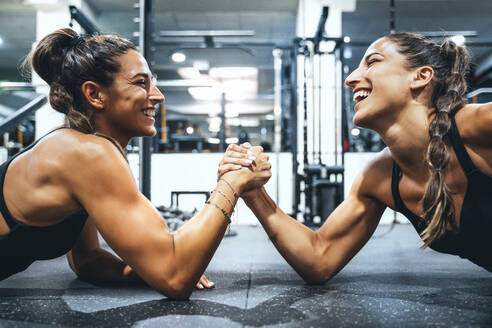 Happy female twins in good shape doing arm wrestling challenge in a gym - JCMF00261