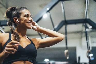 Lächelnde Frau in guter Form mit Kopfhörern in einem Fitnessstudio - JCMF00265