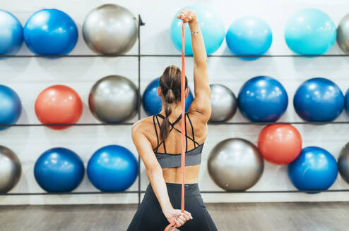 Rückansicht einer Frau in guter Form, die mit einem Fitnessband in einem Fitnessstudio trainiert - JCMF00266