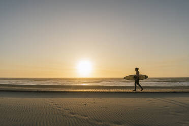 Surfer, der während des Sonnenuntergangs am Strand mit dem Surfbrett spazieren geht - AHSF01046