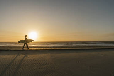 Surfer, der während des Sonnenuntergangs am Strand mit dem Surfbrett spazieren geht - AHSF01048