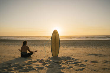 Rückansicht eines Surfers bei der Meditation während des Sonnenuntergangs am Strand - AHSF01051