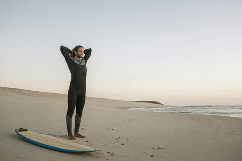 Portugal, Costa Nova, Surfer zieht Neopren an und steht am Strand - AHSF01052
