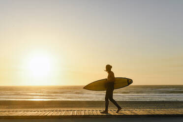 Surfer, der während des Sonnenuntergangs am Strand mit dem Surfbrett spazieren geht - AHSF01057