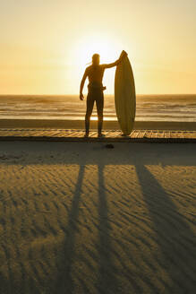 Surfer stehend mit dem Surfbrett in den Sonnenuntergang am Strand - AHSF01059