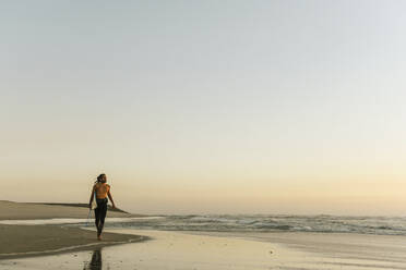 Surfer beim Spaziergang während des Sonnenuntergangs am Strand - AHSF01060