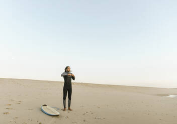 Portugal, Costa Nova, Surfer zieht Neopren an und steht am Strand - AHSF01063